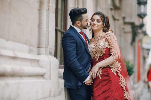 Beautiful woman in a long red dress walks around the city with her husband in a blue suit and with a beard